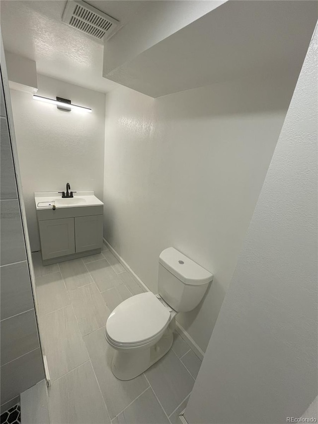 bathroom with toilet, baseboards, vanity, and visible vents