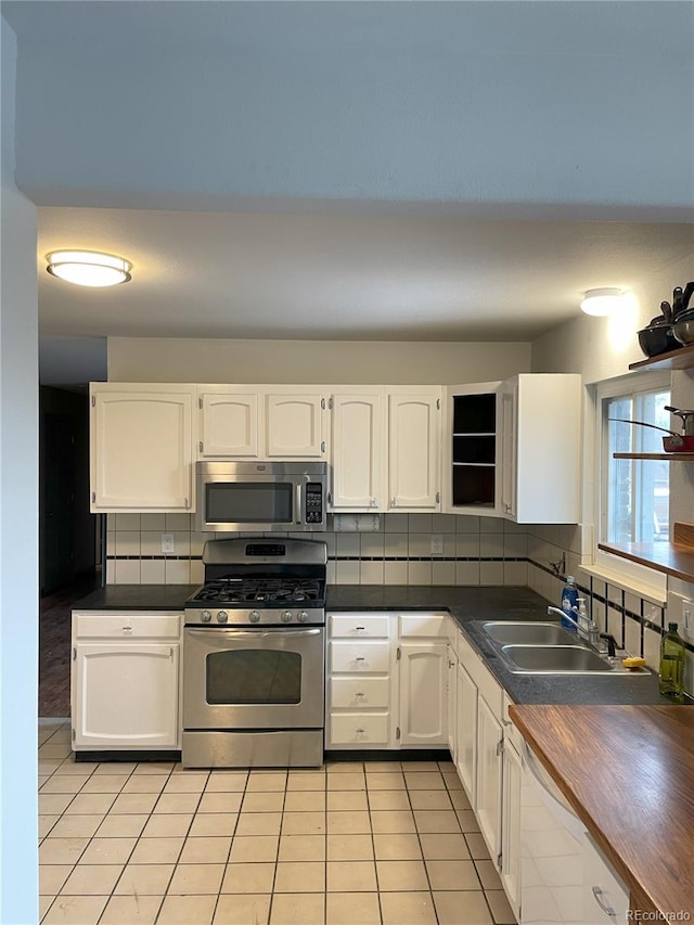 kitchen with stainless steel appliances, dark countertops, light tile patterned floors, and white cabinets