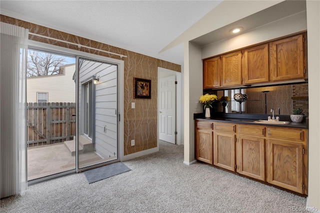 kitchen with light colored carpet, a sink, vaulted ceiling, brown cabinets, and dark countertops