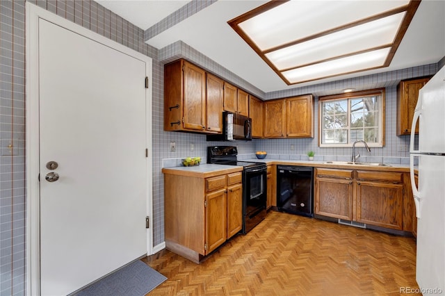 kitchen featuring a sink, light countertops, decorative backsplash, black appliances, and brown cabinetry