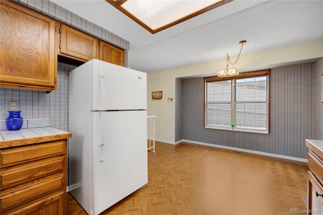 kitchen featuring tile countertops, baseboards, brown cabinets, and freestanding refrigerator