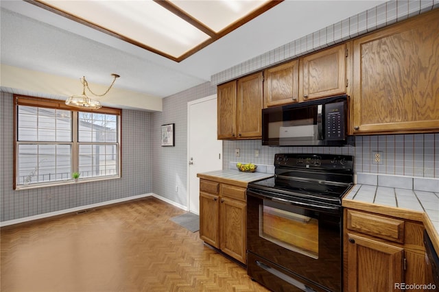 kitchen featuring tile countertops, black appliances, wallpapered walls, and baseboards