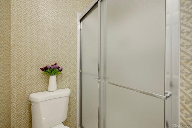 bathroom featuring a shower with shower door, toilet, and wallpapered walls