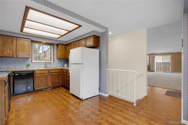 kitchen featuring brown cabinetry, freestanding refrigerator, dishwasher, and a sink