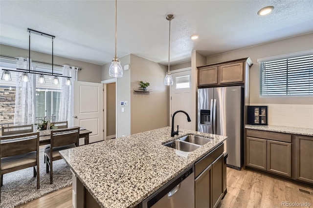 21751 E 7th, Aurora, CO 80018 - kitchen with stainless steel appliances, light wood finished floors, decorative light fixtures, a kitchen island with sink, and tasteful backsplash