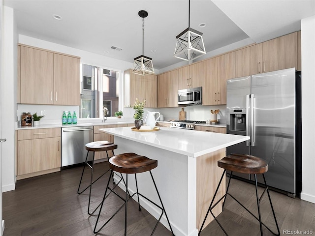 kitchen with appliances with stainless steel finishes, a kitchen island, a kitchen bar, decorative light fixtures, and dark hardwood / wood-style floors