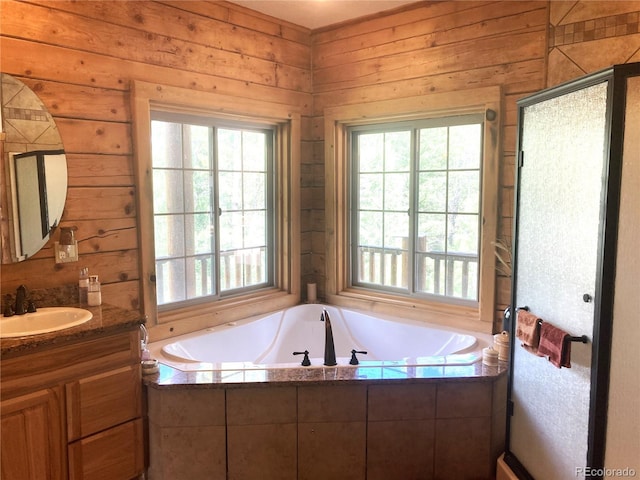 bathroom featuring a wealth of natural light, vanity, wooden walls, and tiled bath