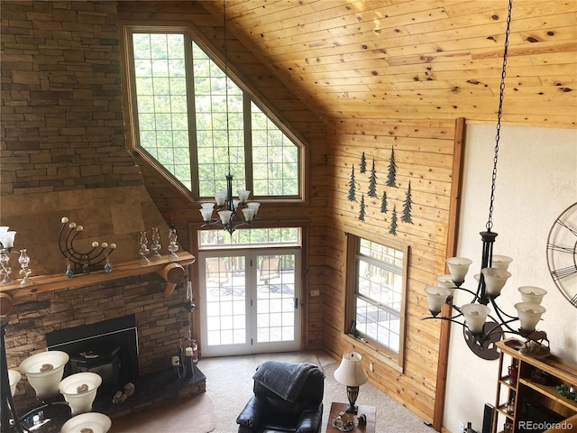 carpeted living room featuring wood walls, a stone fireplace, a notable chandelier, and wood ceiling