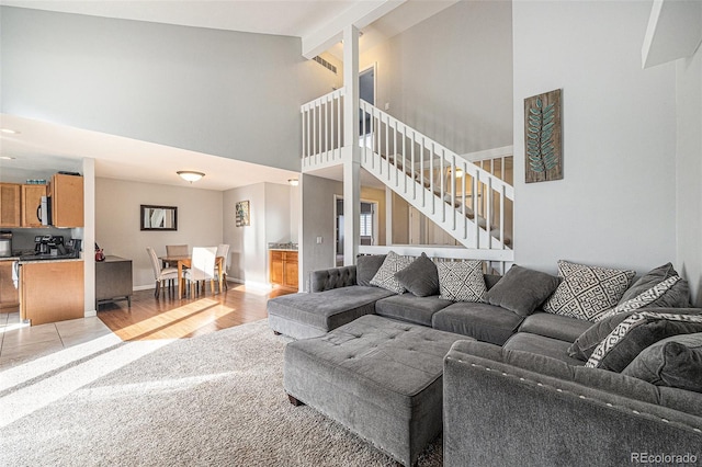 living area with beam ceiling, stairway, light wood-style floors, high vaulted ceiling, and baseboards