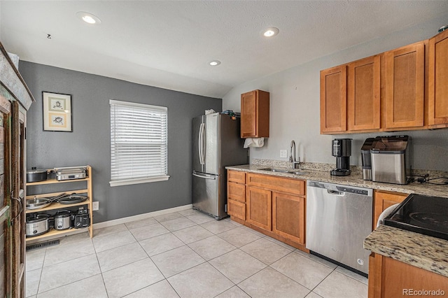 kitchen with brown cabinets, light tile patterned floors, stainless steel appliances, and a sink