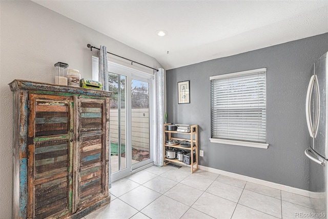 interior space with lofted ceiling, light tile patterned floors, baseboards, and a textured wall