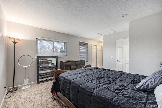 bedroom featuring a closet, attic access, light carpet, a textured ceiling, and baseboards