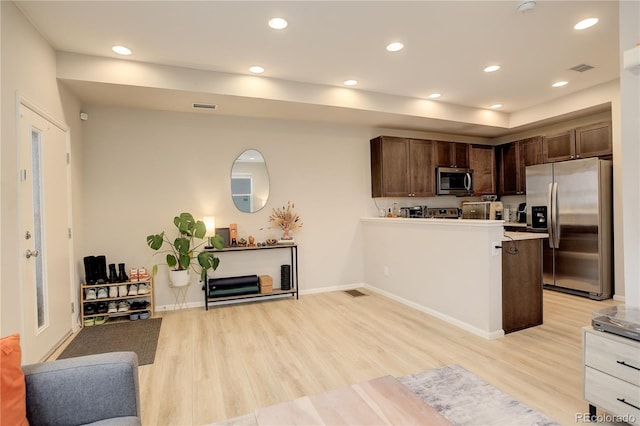 kitchen featuring light countertops, light wood-style flooring, appliances with stainless steel finishes, open floor plan, and a peninsula