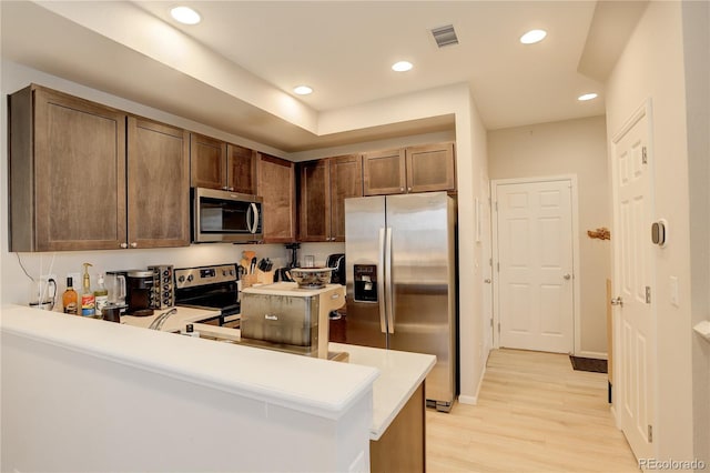 kitchen featuring a peninsula, stainless steel appliances, light countertops, light wood-style floors, and recessed lighting