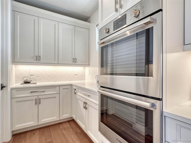 kitchen featuring light wood finished floors, light countertops, decorative backsplash, stainless steel double oven, and white cabinets