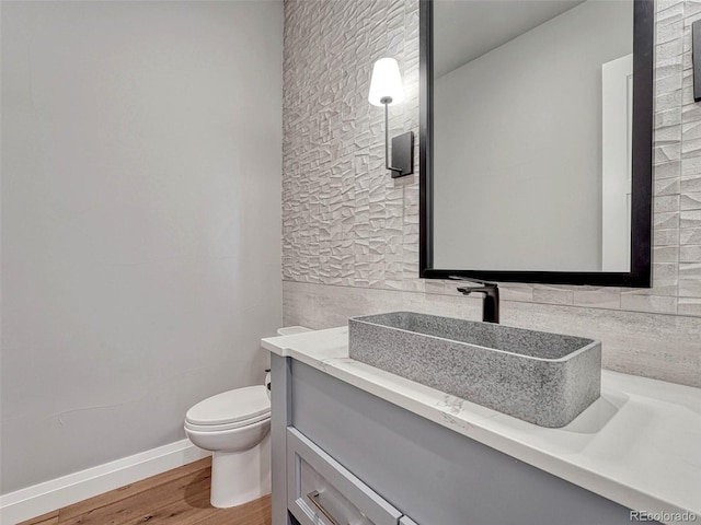 half bath featuring toilet, wood finished floors, tile walls, baseboards, and vanity