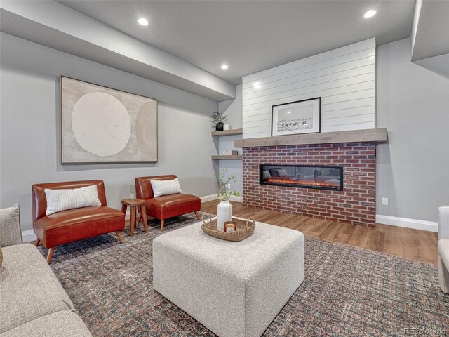 living room featuring a glass covered fireplace, recessed lighting, baseboards, and wood finished floors