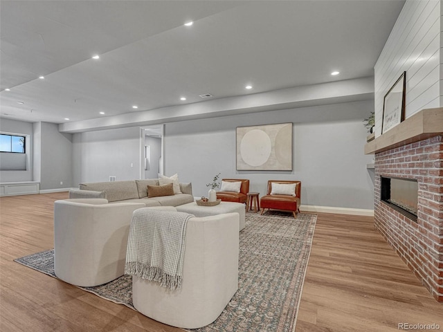 living area featuring recessed lighting, baseboards, a brick fireplace, and wood finished floors