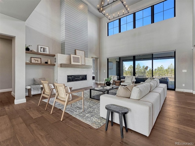 living room featuring baseboards, dark wood-type flooring, an inviting chandelier, and a fireplace