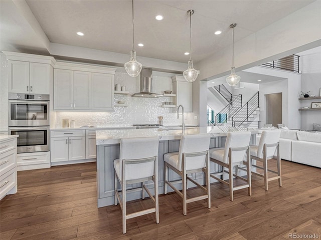 kitchen with open shelves, a sink, dark wood-type flooring, double oven, and wall chimney exhaust hood