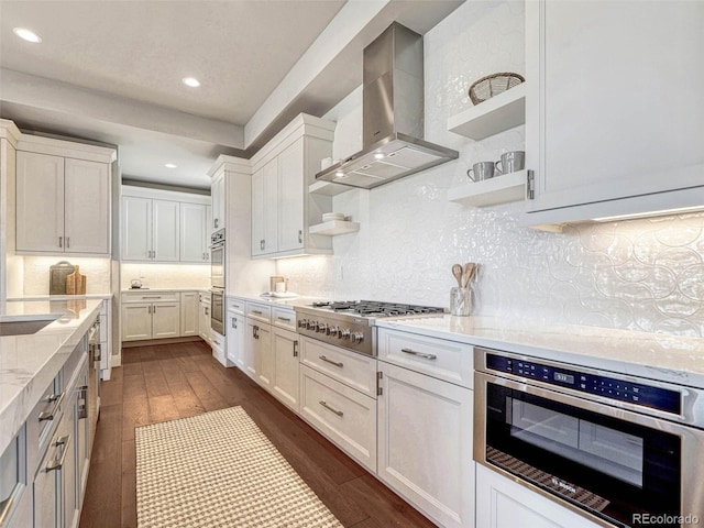 kitchen featuring dark wood-type flooring, wall chimney range hood, appliances with stainless steel finishes, white cabinetry, and open shelves