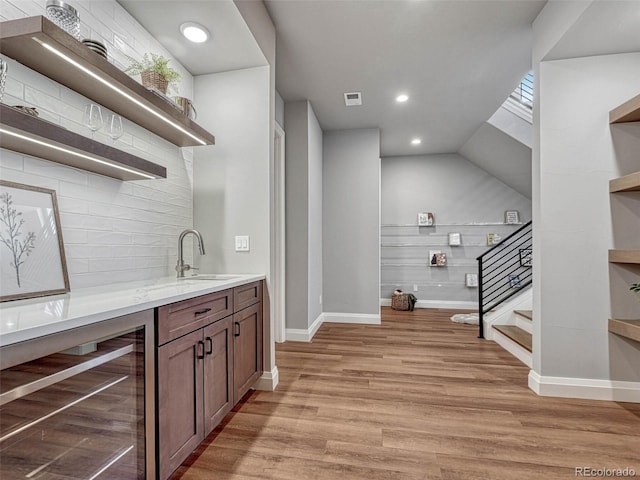 bar with beverage cooler, a sink, tasteful backsplash, light wood finished floors, and stairs