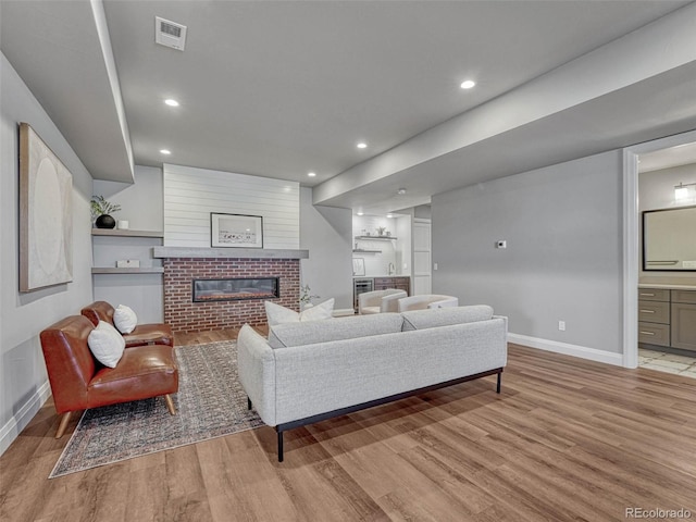 living room featuring recessed lighting, visible vents, light wood-style floors, and a brick fireplace