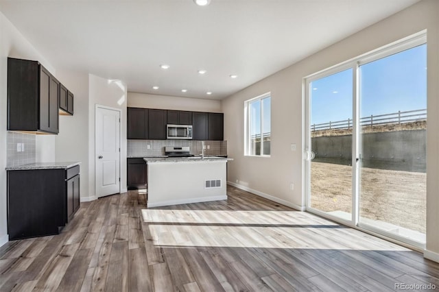 kitchen featuring light stone counters, light hardwood / wood-style floors, a kitchen island with sink, dark brown cabinets, and range