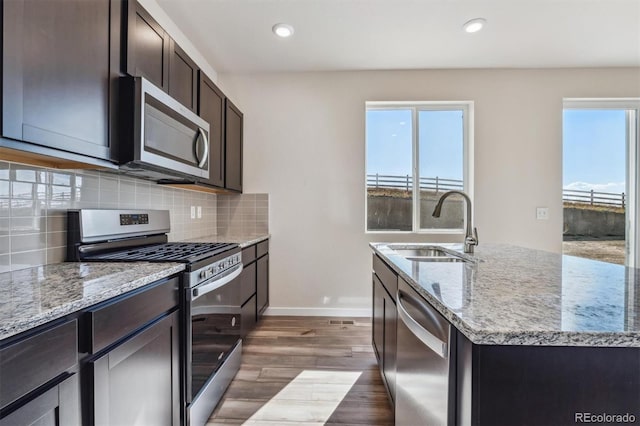 kitchen with light stone countertops, sink, stainless steel appliances, dark hardwood / wood-style floors, and a center island with sink