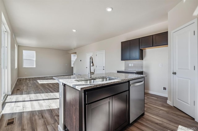 kitchen featuring dark brown cabinetry, light stone countertops, sink, stainless steel dishwasher, and a kitchen island with sink