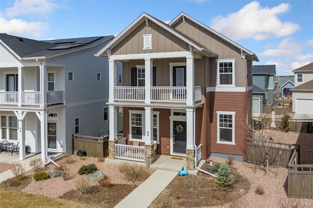 view of front of property with board and batten siding, covered porch, a balcony, and fence