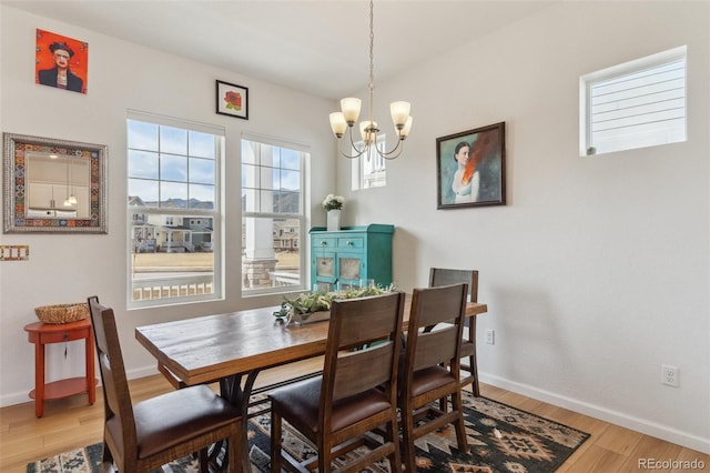 dining space with baseboards, light wood finished floors, and a chandelier