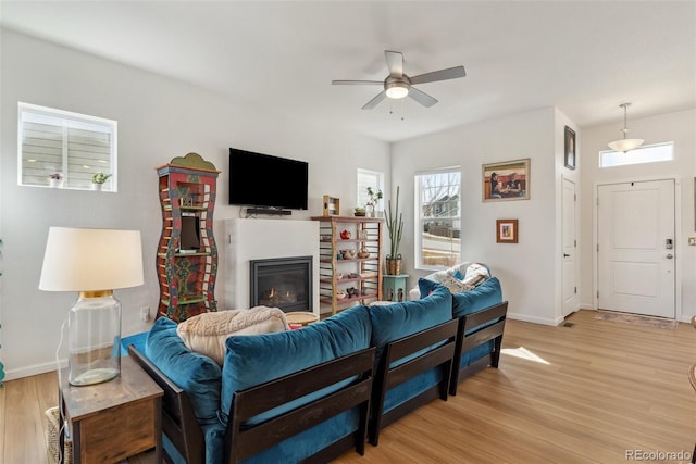 living room featuring a glass covered fireplace, baseboards, light wood-type flooring, and ceiling fan