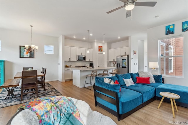 living room featuring recessed lighting, ceiling fan with notable chandelier, and light wood-style floors