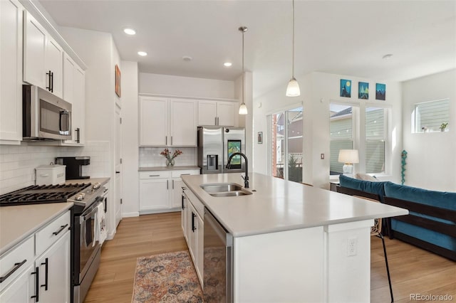 kitchen with light wood finished floors, a sink, stainless steel appliances, open floor plan, and backsplash