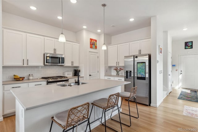 kitchen featuring a breakfast bar area, light wood finished floors, a sink, stainless steel appliances, and white cabinets