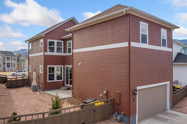 back of property with driveway, an attached garage, and fence