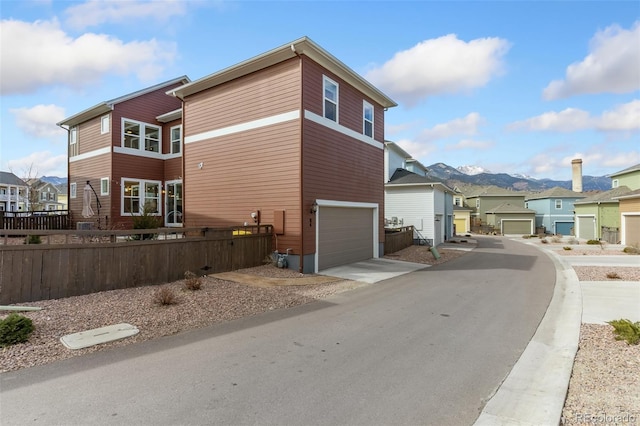 view of property exterior with fence, driveway, an attached garage, a residential view, and a mountain view