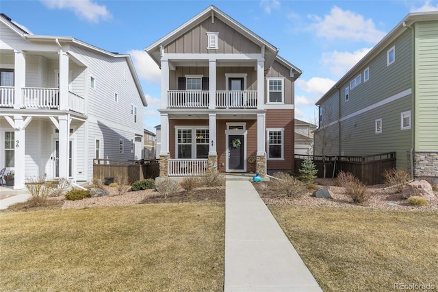 view of front of house featuring a front lawn, stone siding, a porch, board and batten siding, and a balcony