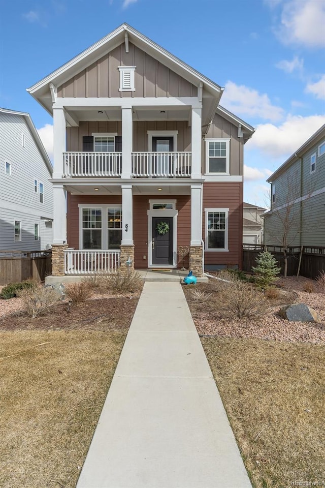 view of front of property featuring stone siding, board and batten siding, a balcony, and fence