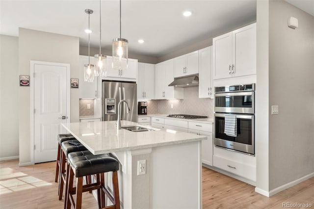 21426 E Stanford Ave, Aurora, CO 80015 - kitchen featuring stainless steel appliances, under cabinet range hood, light wood-style floors, decorative backsplash, and a kitchen island with sink
