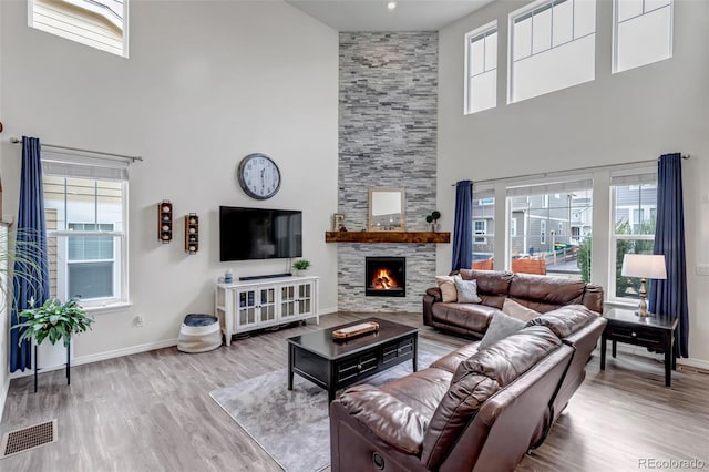 living area with visible vents, wood finished floors, a fireplace, baseboards, and a high ceiling
