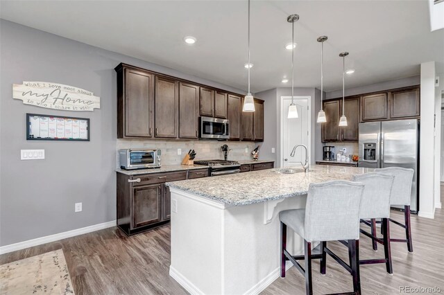 kitchen featuring dark brown cabinetry, backsplash, light stone countertops, a sink, and stainless steel appliances