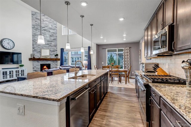 kitchen featuring dark wood-style flooring, appliances with stainless steel finishes, dark brown cabinets, a sink, and light stone counters