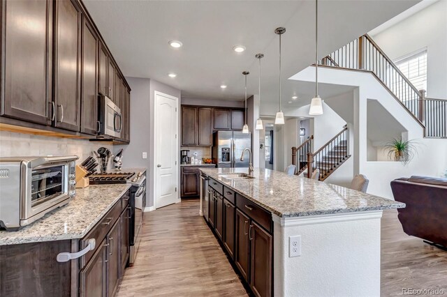 kitchen with dark brown cabinets, appliances with stainless steel finishes, light wood-style floors, a toaster, and backsplash