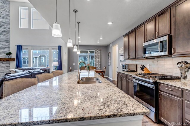 kitchen with light stone countertops, dark brown cabinets, a spacious island, a sink, and stainless steel appliances