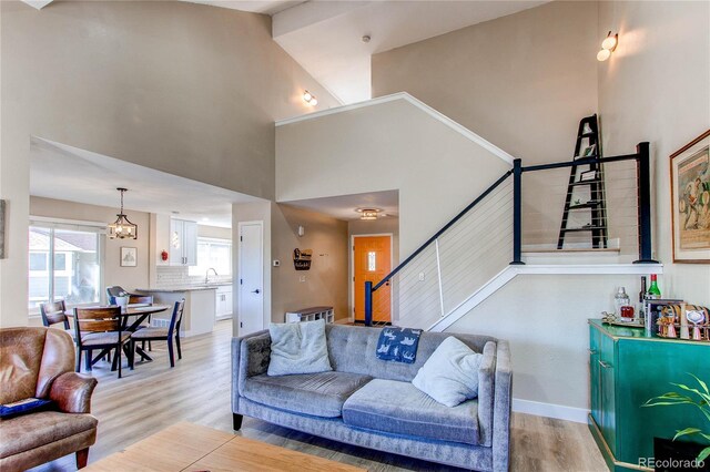 living room featuring high vaulted ceiling, stairway, a chandelier, light wood-type flooring, and baseboards
