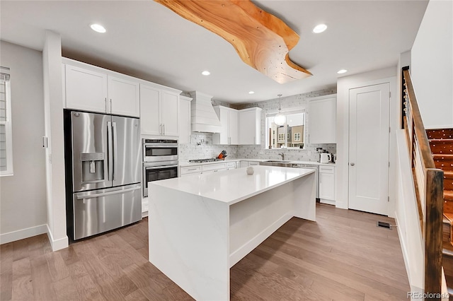 kitchen featuring appliances with stainless steel finishes, custom exhaust hood, light hardwood / wood-style flooring, white cabinets, and a center island