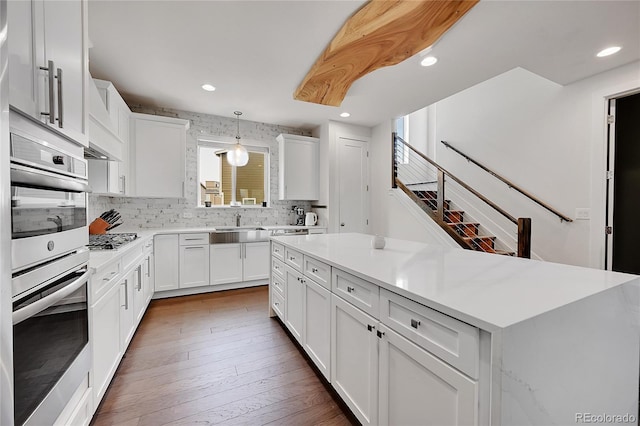 kitchen with pendant lighting, appliances with stainless steel finishes, white cabinets, dark hardwood / wood-style flooring, and decorative backsplash