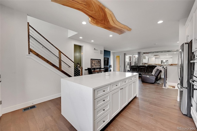 kitchen featuring white cabinets, a kitchen island, light hardwood / wood-style floors, and stainless steel refrigerator